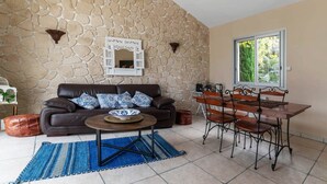 Una sala de estar con una pared de piedra, un sofá de cuero marrón, una mesa de comedor de madera con sillas y una ventana con vistas a zonas verdes.