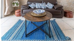 Una sala de estar con una pared de piedra, un sofá de cuero marrón, una mesa de centro y una alfombra azul estampada.