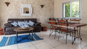 Una sala de estar con una pared de piedra, un sofá de cuero marrón, una mesa de centro, una mesa de comedor con sillas y una ventana con vistas a árboles.
