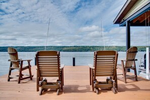 Una terraza de madera con dos sillas Adirondack mirando un lago, un área cubierta a la derecha y un cielo despejado.