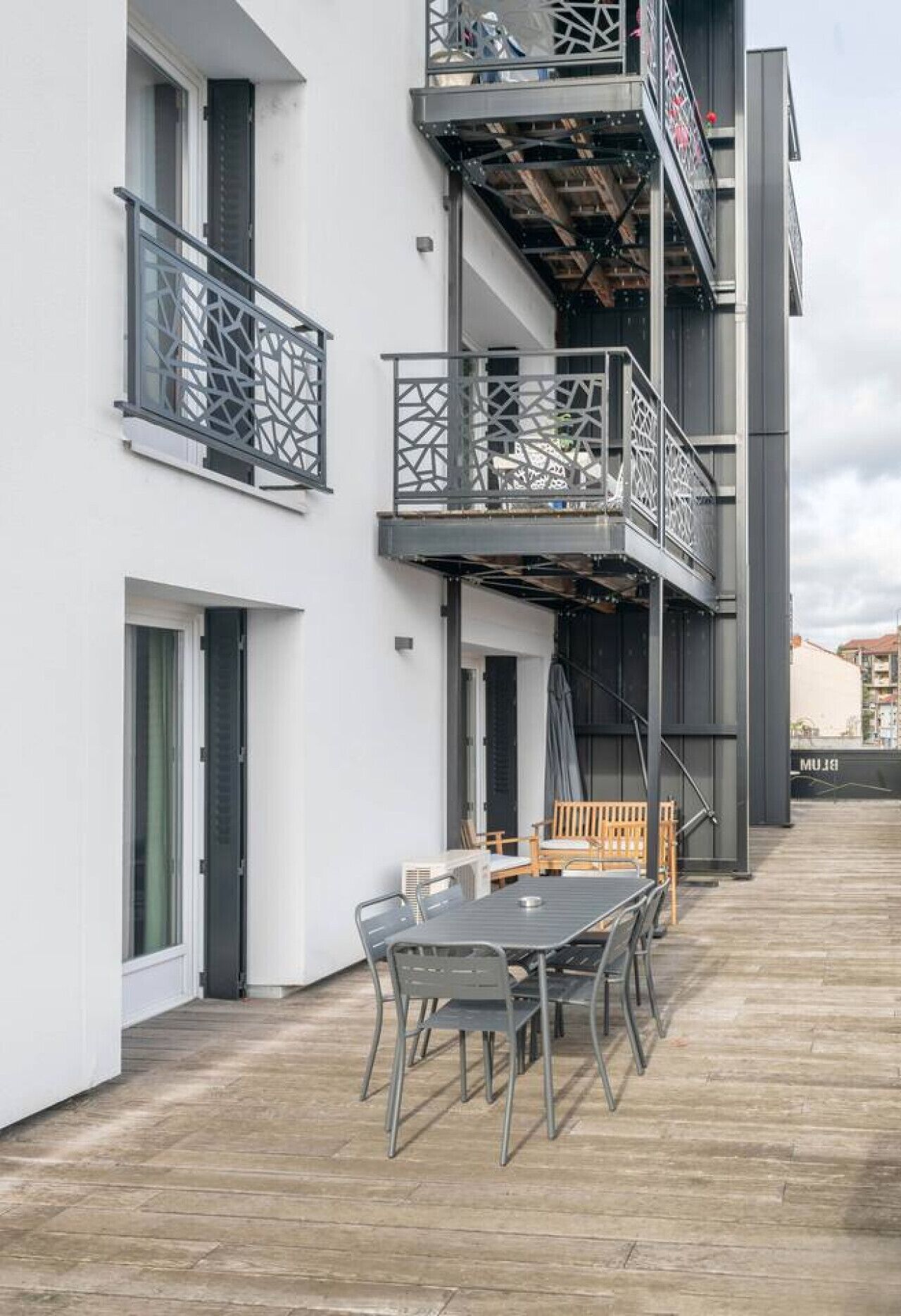 A modern building with a balcony, a table with chairs, and a wooden bench.