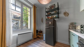 A compact kitchen with a built-in refrigerator, a window with curtains, and a wooden stool.