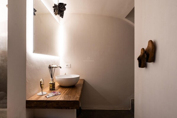Un baño con tocador de madera, lavamanos blanco, espejo y lámpara colgante.