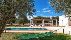 Zona de piscina con sillas de descanso, una hamaca y una pérgola.