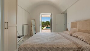 Un dormitorio con una cama grande, un armario, un espejo y vistas a una piscina y jardín.