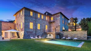 A large stone building with a swimming pool, outdoor seating, and a bell tower in the background. - Palazzo Pozzo Bonelli 14, Emma Villas (Ottiglio)
