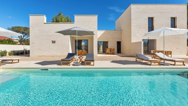 Un espace piscine moderne avec des chaises longues et des parasols, une piscine à eau claire et un bâtiment au design minimaliste.
