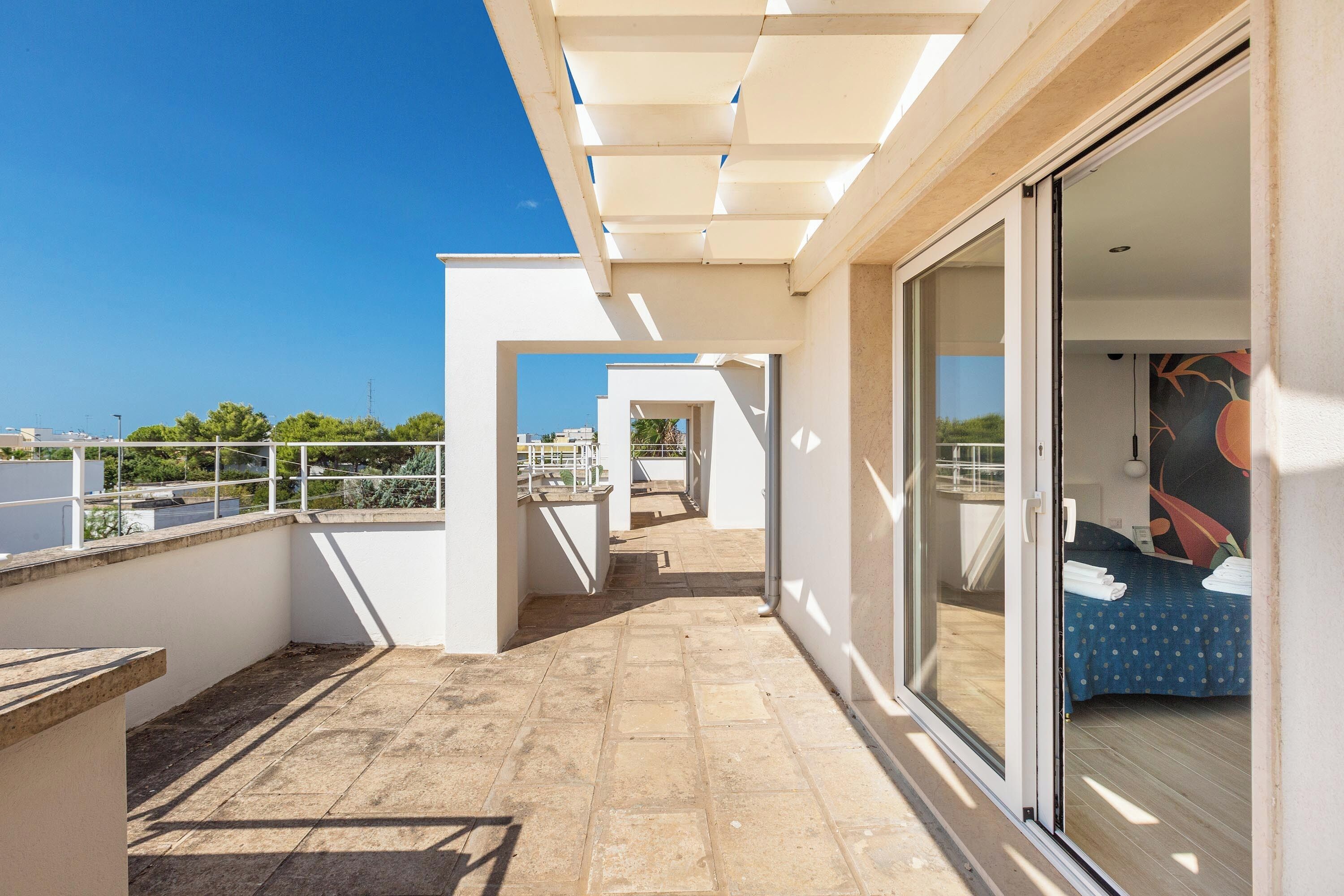 A modern balcony with a clear view of the cityscape, a sliding glass door leading to a bedroom, and a tiled floor.