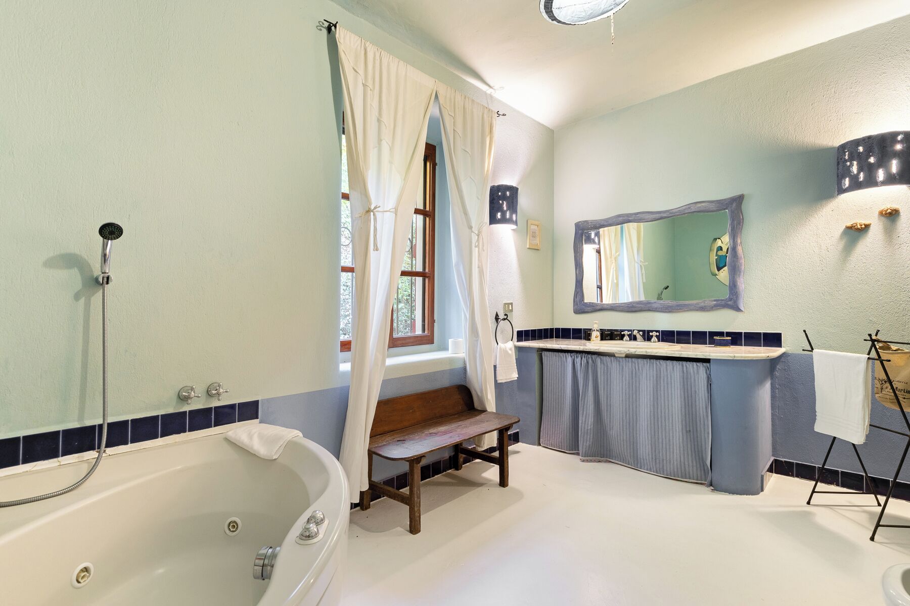 A bathroom with a bathtub, a bench, a sink, and a mirror.