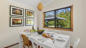 Un coin repas avec une table dressée pour quatre personnes, des œuvres d’art encadrées accrochées au mur et une vue sur l’extérieur grâce à une grande fenêtre.