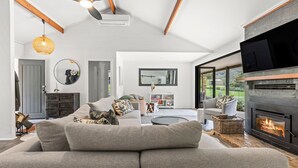 Un salon moderne avec un canapé d’angle, une cheminée et un grand téléviseur fixé au mur.
