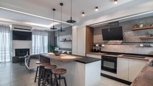 A modern kitchen with a central island, bar stools, a built-in oven, and a large flat-screen TV mounted on the wall.