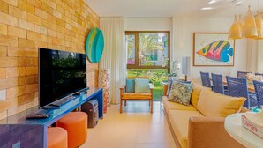 Una sala de estar con televisor, sillones naranjas, sofá y comedor con sillas de mimbre.