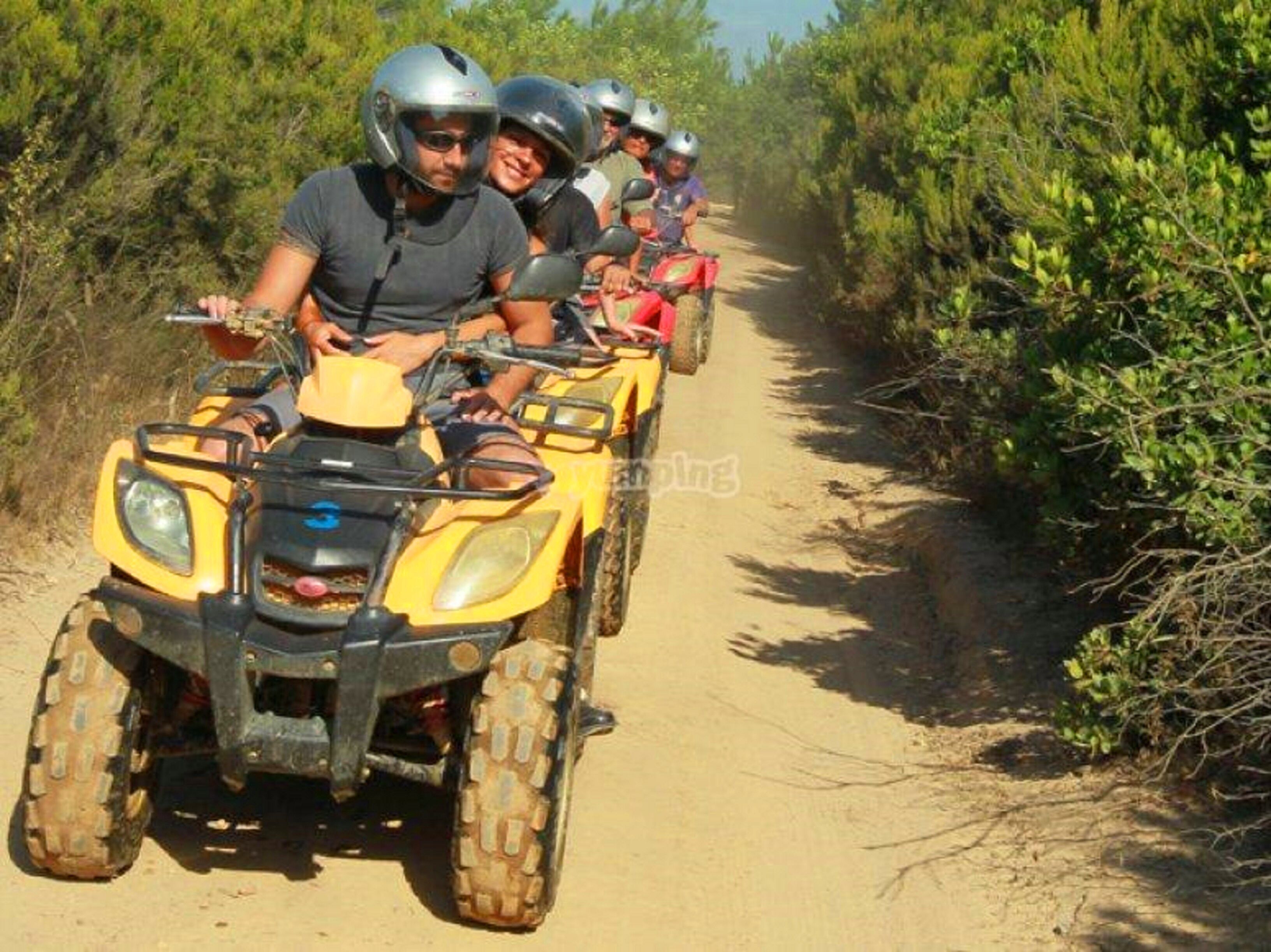 Un groupe de personnes circulant en quads sur un chemin de terre, entouré de verdure.