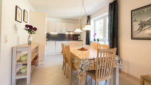 Un coin repas avec une table et des chaises en bois, un vase rempli de fleurs et, au fond, une cuisine.