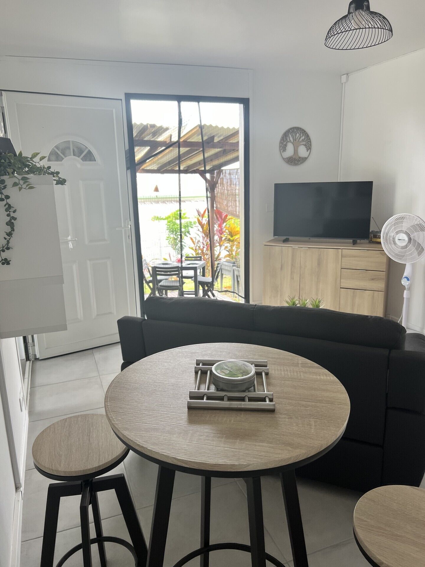 A modern living room with a round table, two stools, a black sofa, a television, and a fan.
