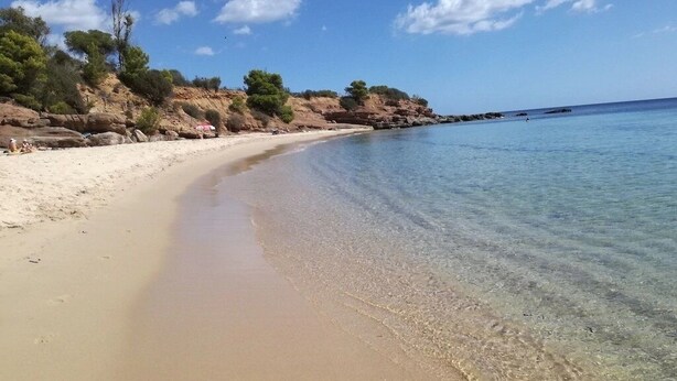 A beach with clear water, sandy shore, and rocky outcrops.
