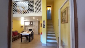 A spacious living area with a high ceiling, a dining table, and a staircase leading to an upper level.
