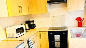 A compact kitchen with wooden cabinets, a microwave, a coffee maker, an oven, and a dishwasher. - Convenient Home - Sleeps 6 - Parking - Garden (Northampton)