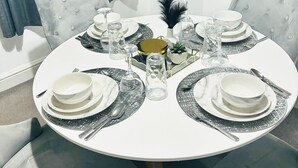 A round dining table set with white plates, silverware, and glassware, surrounded by tufted chairs. - Convenient Home - Sleeps 6 - Parking - Garden (Northampton)