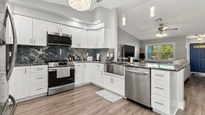 A modern kitchen with white cabinetry, a marble countertop, stainless steel appliances, and a chandelier. - Jacks Blue Haven- 3/2 Heated Pool, Game Room & Close to Gulf Beaches!!  (Largo)