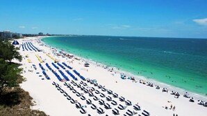 A beach with rows of beach umbrellas and sun loungers, a clear blue sky, and a calm sea. - Jacks Blue Haven- 3/2 Heated Pool, Game Room & Close to Gulf Beaches!!  (Largo)
