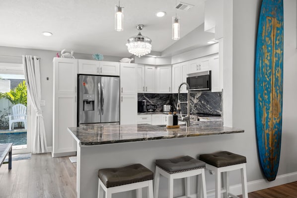A modern kitchen with white cabinets, stainless steel appliances, and a marble countertop.