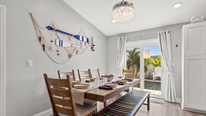 A dining area with a wooden table set for four, surrounded by wooden chairs. A colorful bench is placed in front of the table. - Jacks Blue Haven- 3/2 Heated Pool, Game Room & Close to Gulf Beaches!!  (Largo)