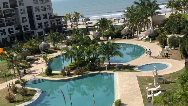 Un resort con una grande area piscina, palme e vista sull'oceano.