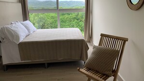 Una camera da letto con un letto, una sedia, una finestra vista su dolci colline e uno specchio fissato alla parete.