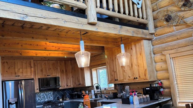 A spacious kitchen with wooden cabinets, a stainless steel refrigerator, a microwave, and a coffee maker. There is a wooden dining table with chairs and a dog bowl on the floor.