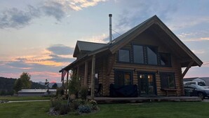 A log cabin with a large porch, a chimney, and a view of the surrounding landscape.