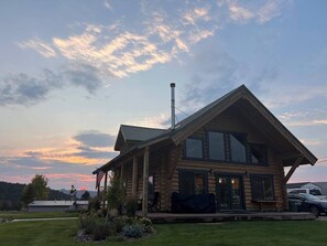 A log cabin with a large porch, a chimney, and a view of the surrounding landscape. - Dutch John Adventure Outpost—2800 Sq Ft, log home, private Pickleball Court.<br>Best short term rental in Dutch John! (Dutch John)