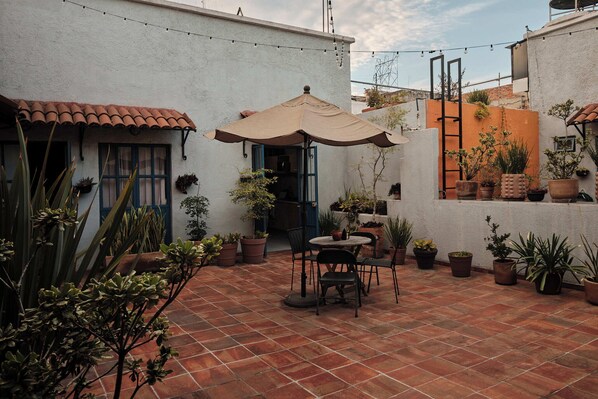 Un patio con una mesa y sillas, rodeado de plantas en macetas y una guirnalda de luces.