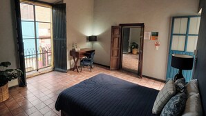 Een slaapkamer met een bed, een bureau en een stoel. Er is een raam met uitzicht op gebouwen.