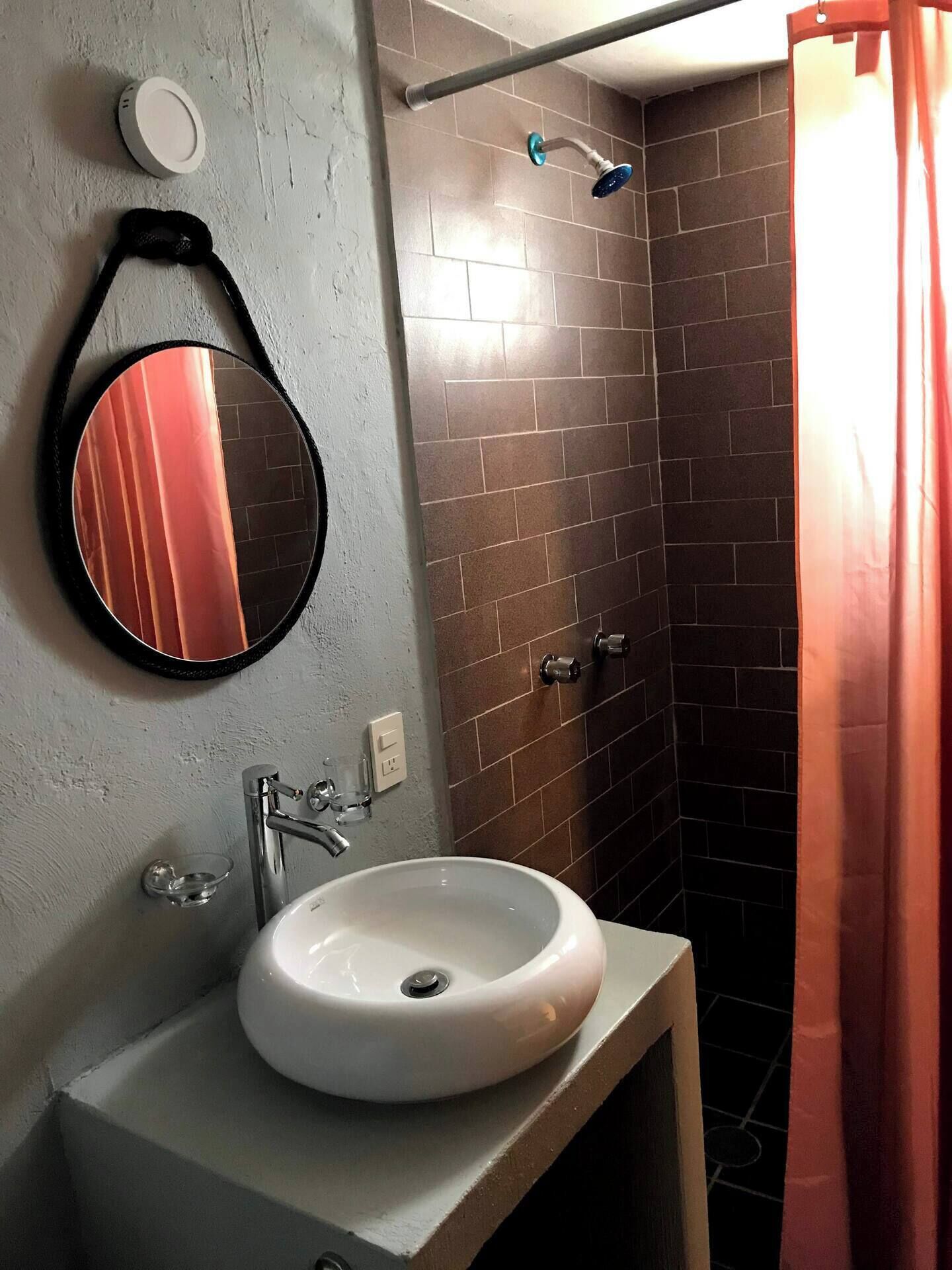 A bathroom with a white sink, a round mirror, a shower with a handheld showerhead, and a towel rack.