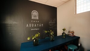 A bar area with a chalkboard displaying the name 'CASA ARRAYÁN' and a logo. There are two stools, a table with a stack of books, and two vases with plants. - Casa Arrayán 3 Private Room / Private Bathroom  (Guadalajara)