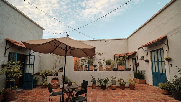 An outdoor patio with a table and chairs under a large umbrella, surrounded by potted plants and string lights. - Casa Arrayán 3 Private Room / Private Bathroom  (Guadalajara)