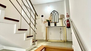 A staircase with wooden steps and a metal railing, leading to a room with a white wall, a small table with a vase, and a fire extinguisher. - Casa Augusta 6 (Braga)