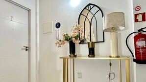A room with a white door, a console table with a lamp, a mirror, and a vase with flowers. - Casa Augusta 6 (Braga)