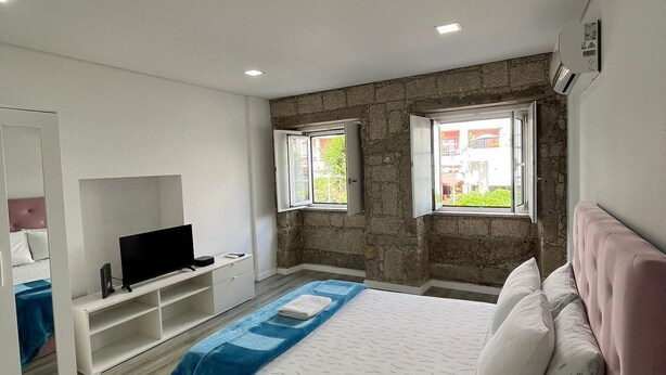 A bedroom with a bed, a TV, a wardrobe, and a stone wall. - Casa Augusta 6 (Braga)