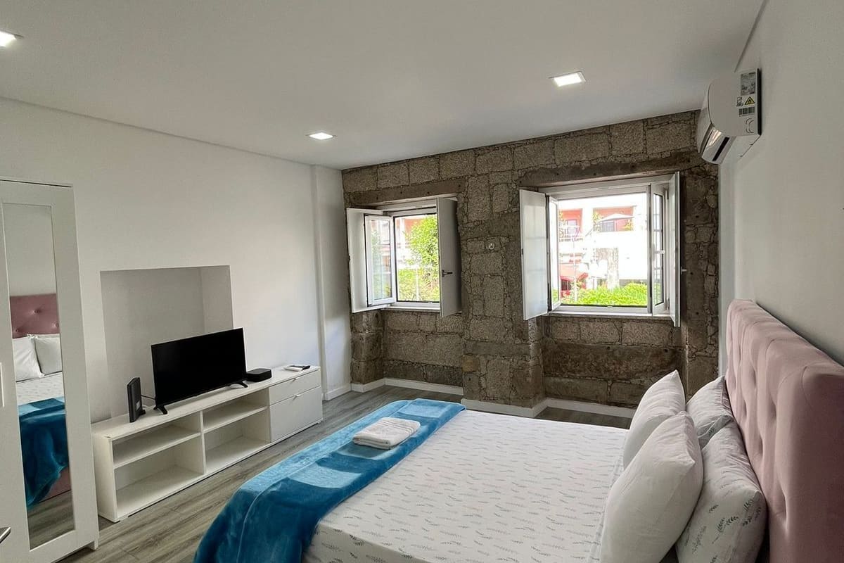 A bedroom with a bed, a TV, a wardrobe, and a stone wall.