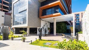 A modern building with a glass facade, outdoor seating area, and greenery. - Flat Way Style - By Almare (João Pessoa)