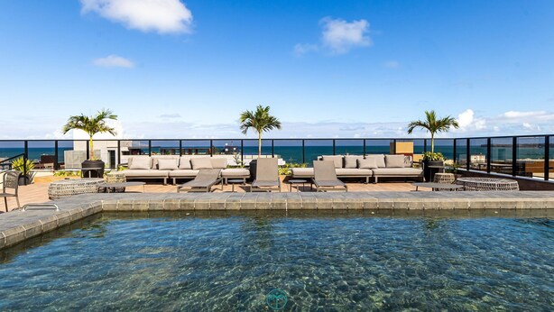 A rooftop pool area with clear water, lounge chairs, and palm trees, overlooking the ocean. - Flat Way Style - By Almare (João Pessoa)