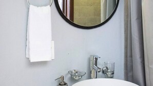 Een badkamer met een ronde spiegel, een wit wastafel, een handdoekhouder en een zeepdispenser.