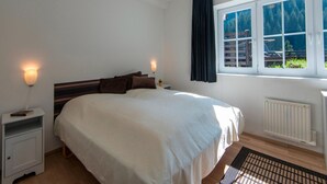 A bedroom with a large bed, bedside lamps, a window with a view of greenery, and a radiator. - Apartment in Bad Gastein Near Ski Slopes (Bad Gastein)