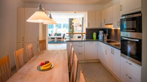 A modern kitchen with white cabinets, a dining table with chairs, and a hanging light fixture. - Apartment in Bad Gastein Near Ski Slopes (Bad Gastein)