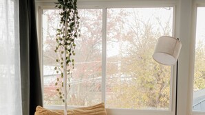 A cozy room with a large window, a sofa, a small table with a cup and book, and a hanging plant. - Your Cozy Getaway with Sunroom & Gaming Room (Streamwood)