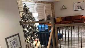 A staircase with a wooden handrail and black metal balusters, leading to a living area with a blue chair and a Christmas tree. - Your Cozy Getaway with Sunroom & Gaming Room (Streamwood)