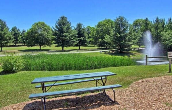 Une table de pique-nique dans un parc, avec une fontaine et des arbres en arrière-plan.